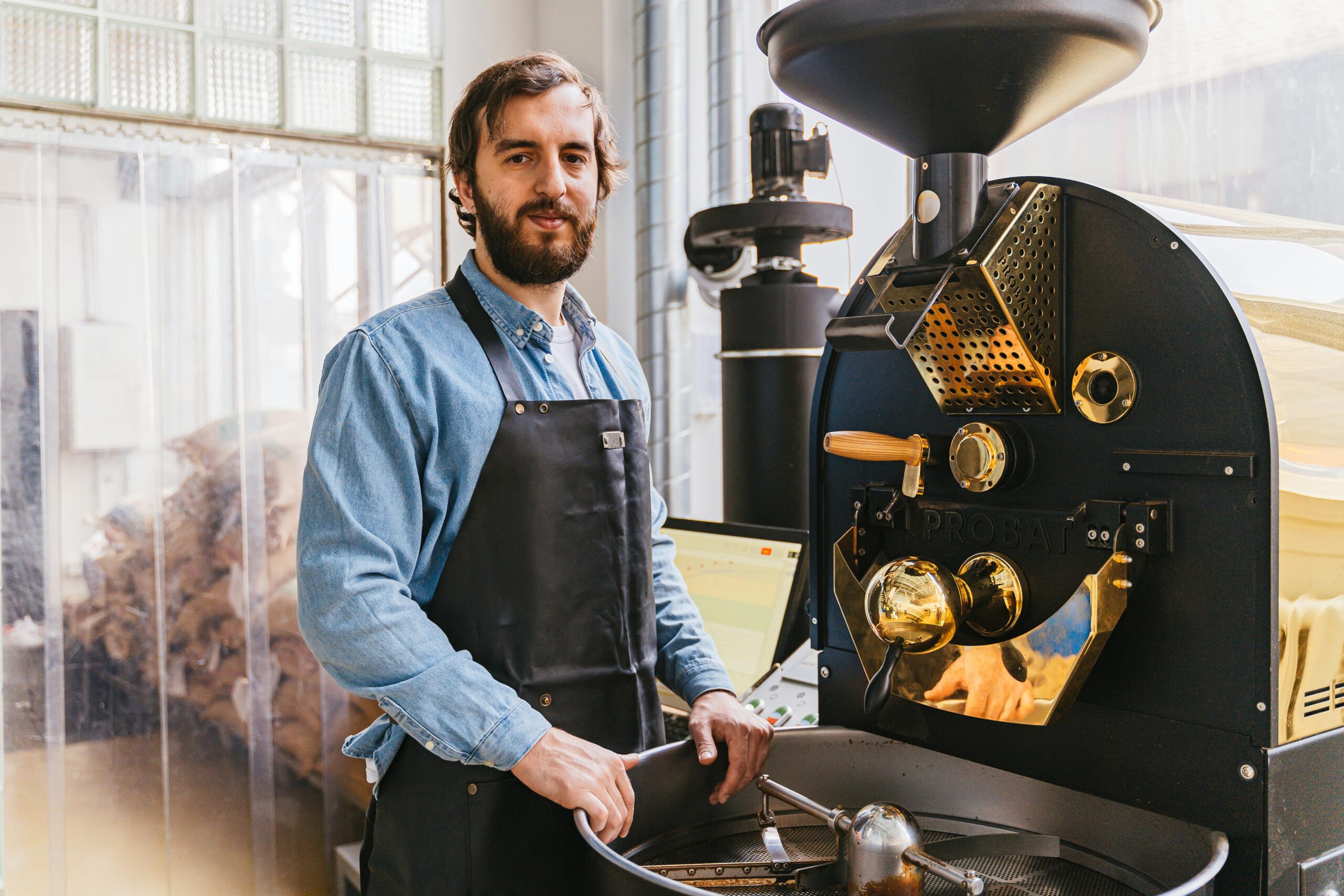 Bearded man working with a coffee roaster in a modern workshop. Indoor setting.